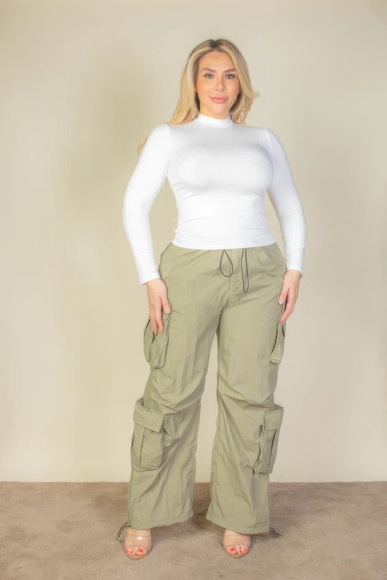Plus size model wearing khaki parachute pants with flap pockets and drawstring, styled with a white top.