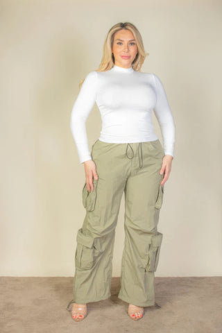 Plus size model wearing khaki parachute pants with flap pockets and drawstring, styled with a white top.