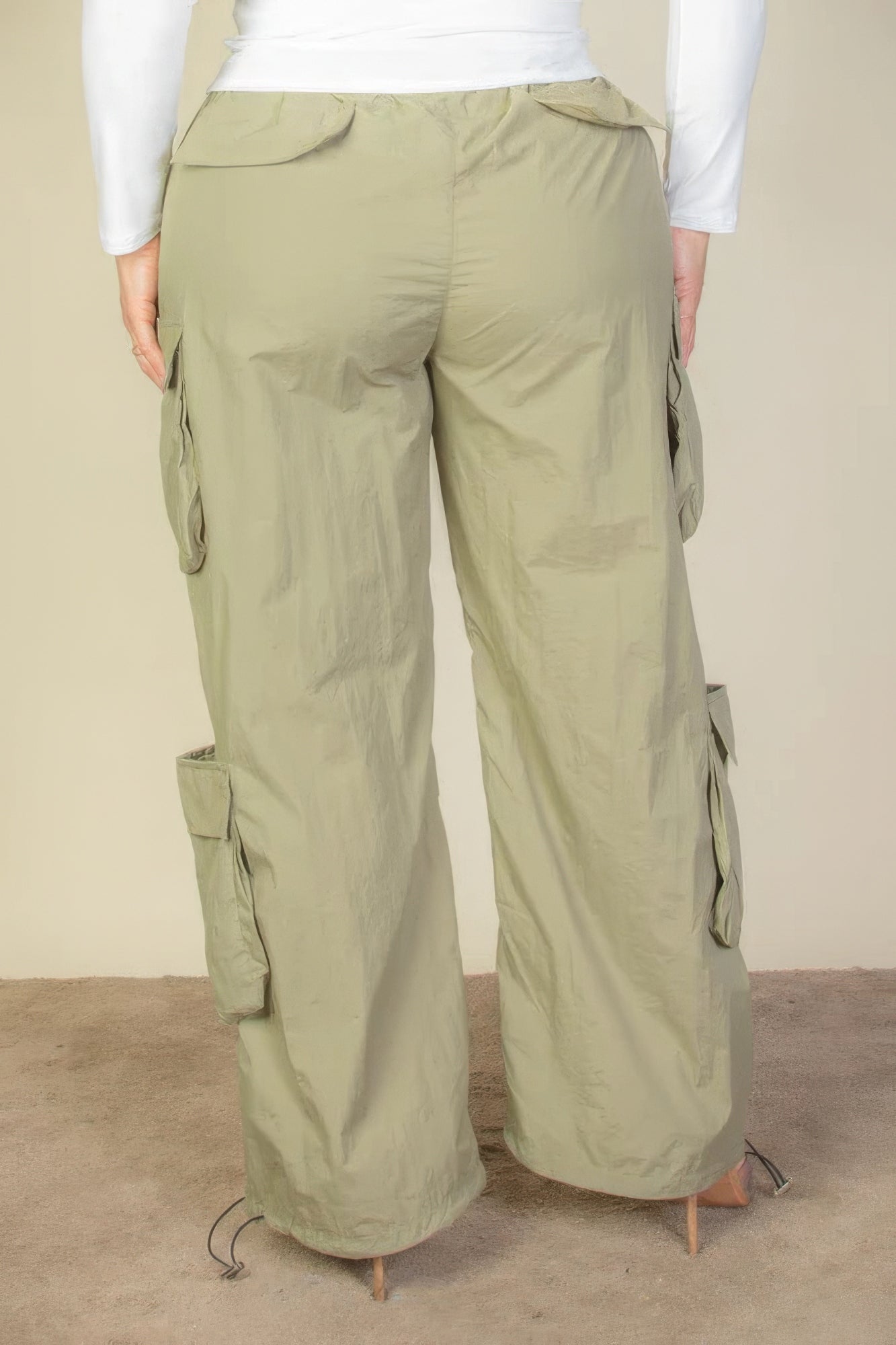 Plus size nylon parachute pants with flap pockets and drawstring, shown in light green, highlighting rear view and ruched detailing.