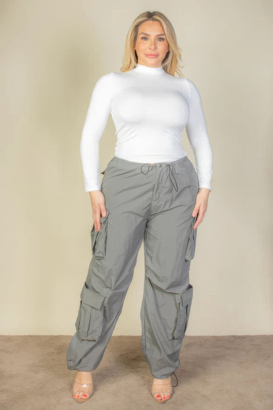 Woman wearing plus size grey parachute pants with flap pockets and drawstring waist, paired with a white top.