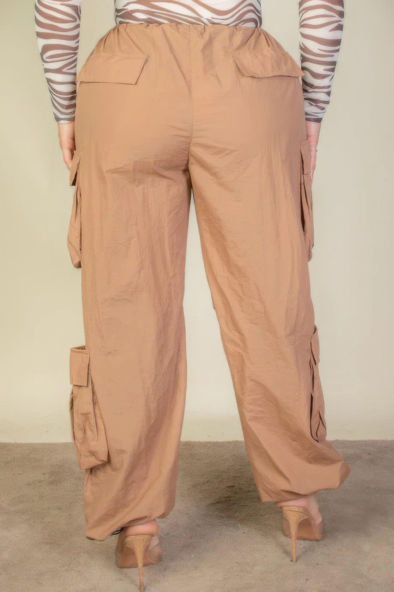 Plus size beige parachute pants with flap pockets and drawstring, shown from the back, highlighting ruched details and fit.