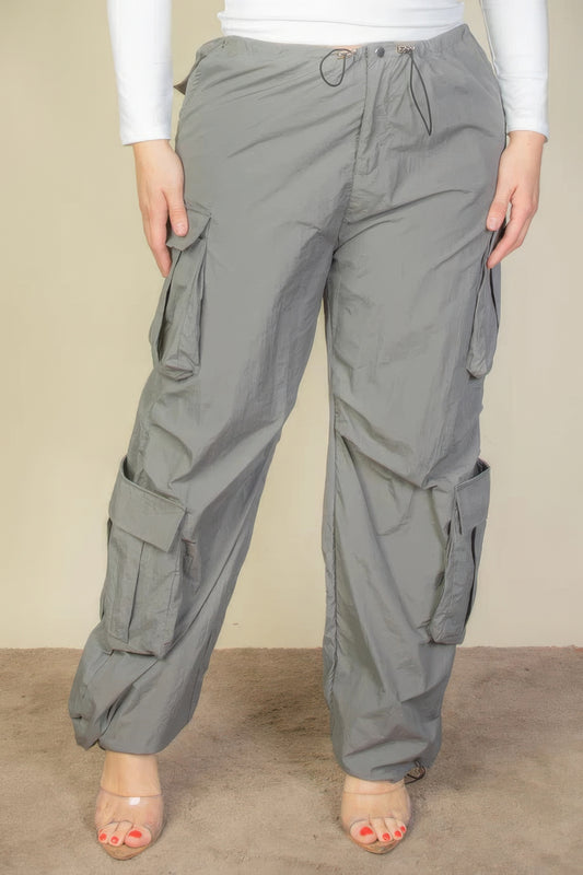 Plus size grey nylon parachute pants with flap pockets and drawstring ruching, shown for versatile style and comfort.