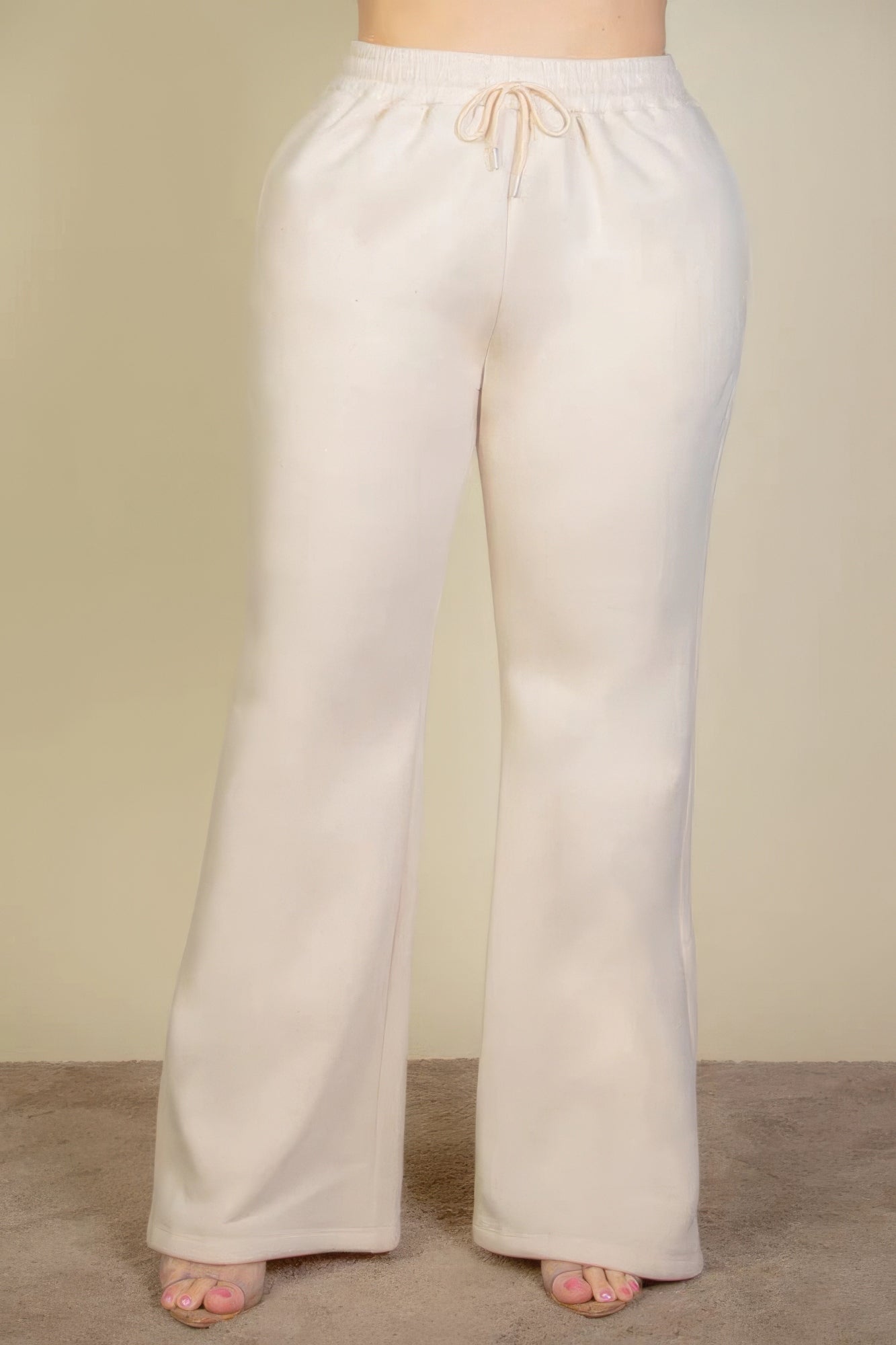 Plus size sweatpants with drawstring waist and slant pockets in cream color, featuring a bootcut silhouette and soft fabric.