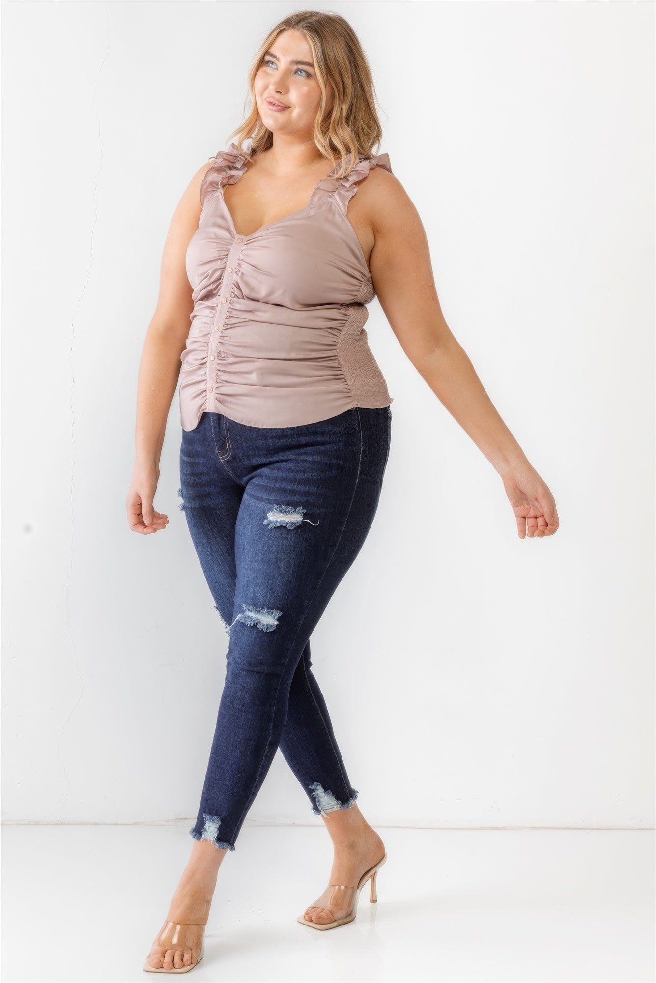 Plus size model wearing mauve ruched button-up ruffle strap tank top with smocked back, paired with dark jeans and heels.