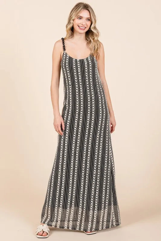 Young woman with blonde hair smiling, wearing a black and white patterned maxi dress with thin straps, standing against a beige background.