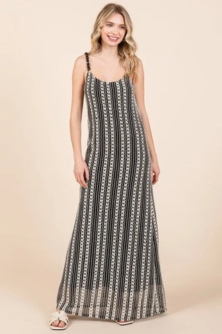 Young woman with blonde hair smiling, wearing a black and white patterned maxi dress with thin straps, standing against a beige background.