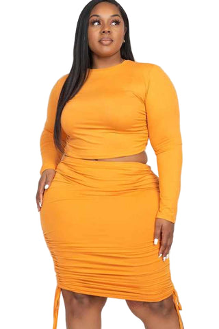 Plus size model wearing orange two-piece skirt set with ruched crop top and drawstring skirt made from high stretch jersey material.