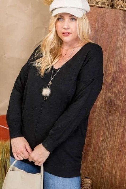 Plus size model wearing a black V-neck hi-lo sweater with 3/4 sleeves, paired with a white hat and necklace.