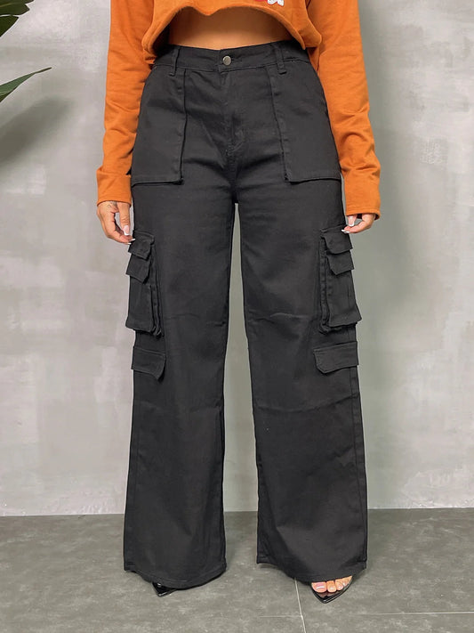 Plus size black wide leg cargo pants with utility pockets, styled with an orange top on a concrete background.