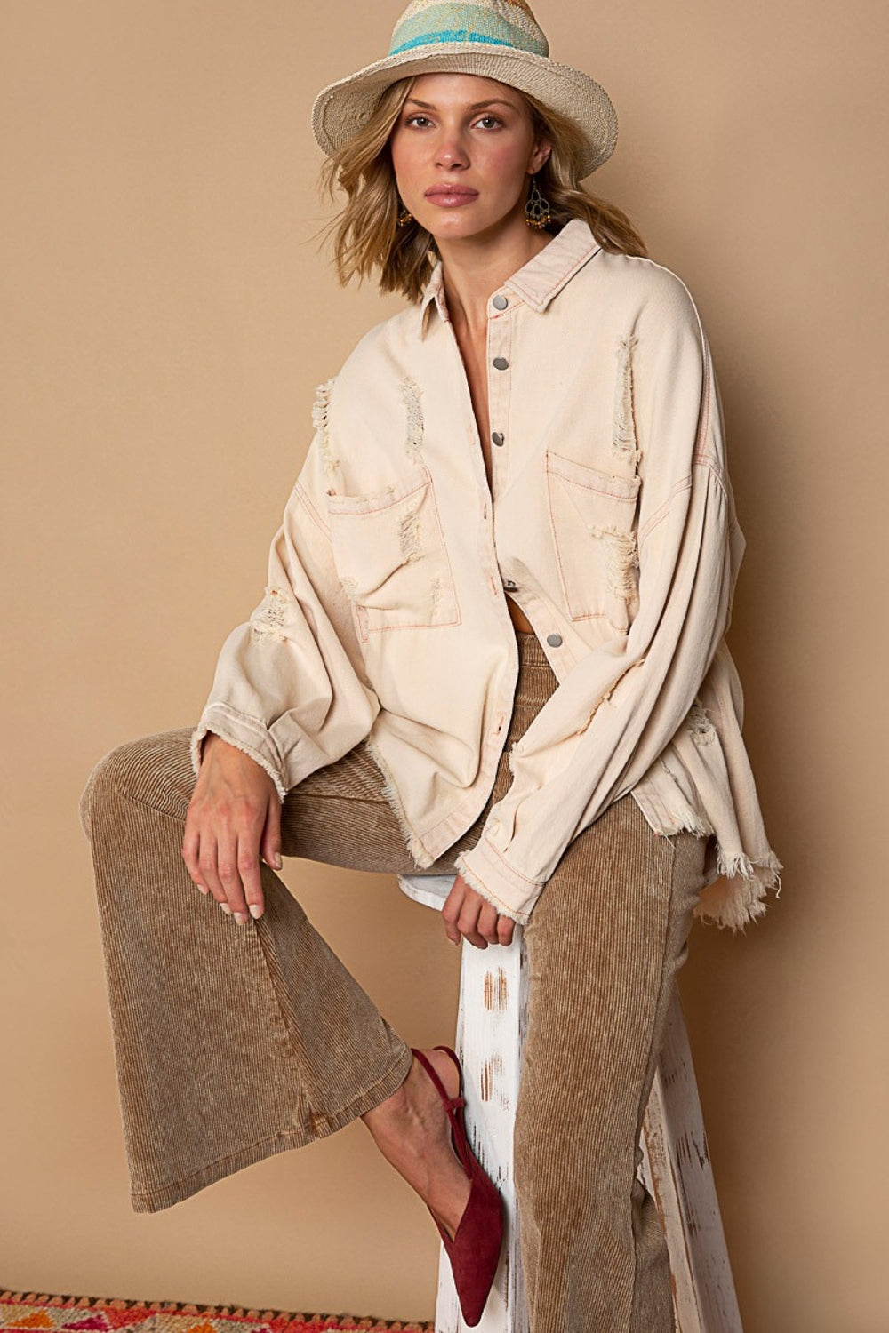 Woman in pink beige distressed shacket with raw hem, styled with wide-leg pants and hat, showcasing a trendy layered outfit.