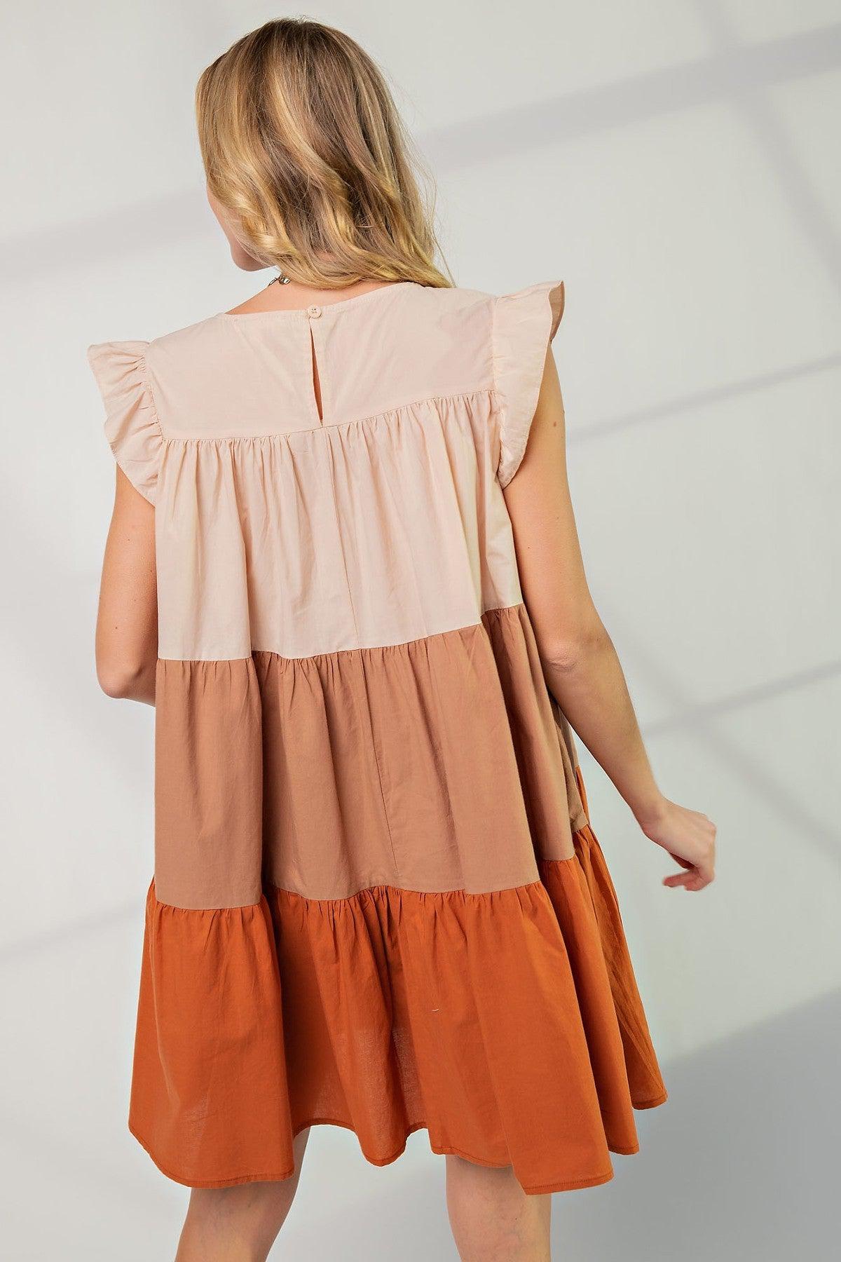 Woman wearing a poplin tiered color block dress with boat neckline and ruffle sleeves, showcasing autumn shades and flowy design.