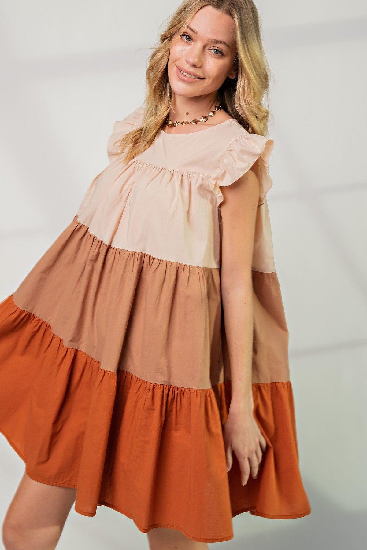 Woman wearing flowy poplin tiered color block dress with boat neckline and ruffle sleeves, featuring autumn hues and loose fit.