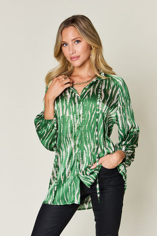Woman wearing green printed button-up long sleeve shirt with frill design, 100% polyester, paired with dark pants.