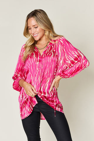 Woman wearing a vibrant pink printed button-up long sleeve shirt with frill details, made of 100% polyester, paired with black pants.