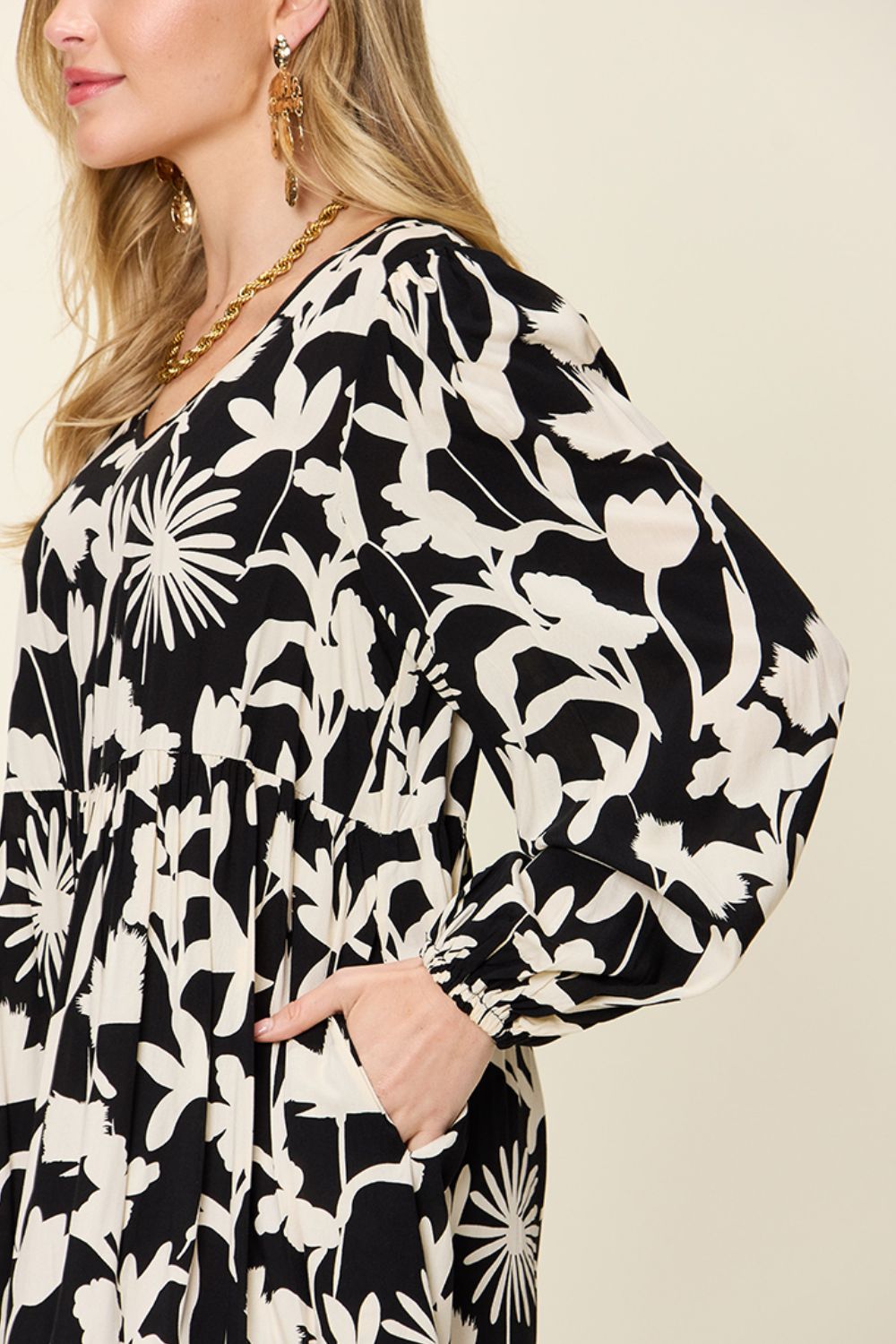 Woman wearing a black and white printed ruffle hem dress with pocket and floral design.