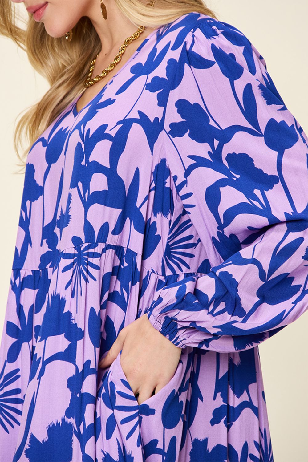 Woman wearing a printed ruffle hem dress with a pocket, featuring a vibrant floral design in blue and purple, made of 100% rayon.