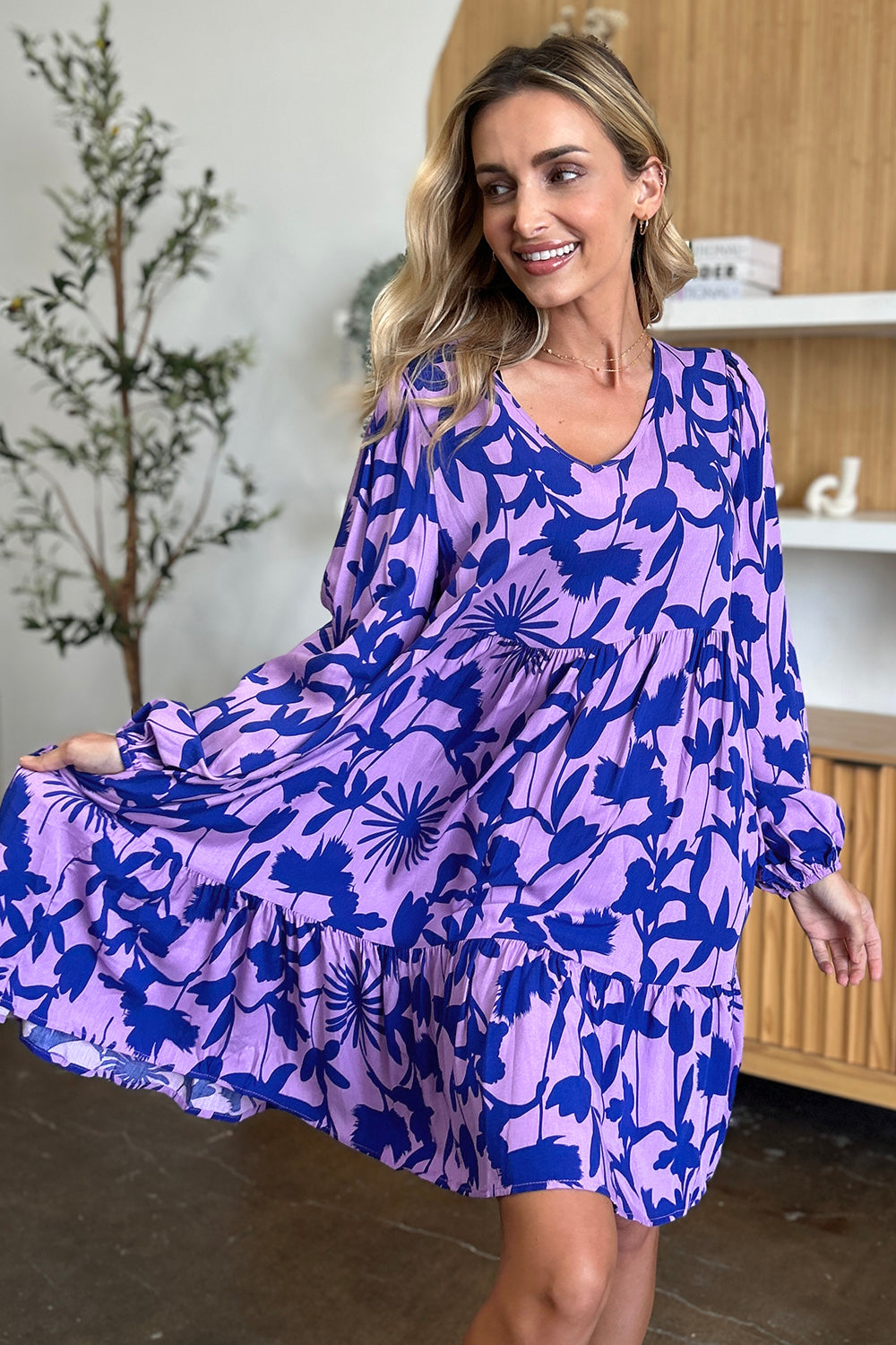 Woman wearing a printed ruffle hem dress with floral design, showing the pocket detail in a stylish indoor setting.