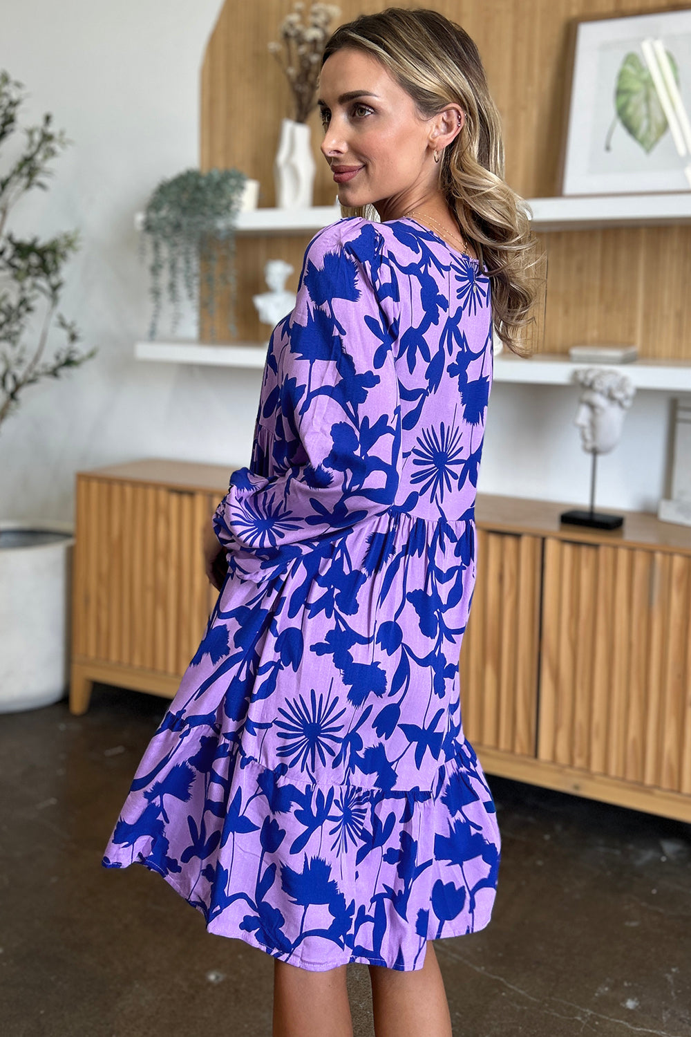 Woman wearing a printed ruffle hem dress with pockets, showcasing a vibrant floral design in blue and purple, perfect for a stylish look.