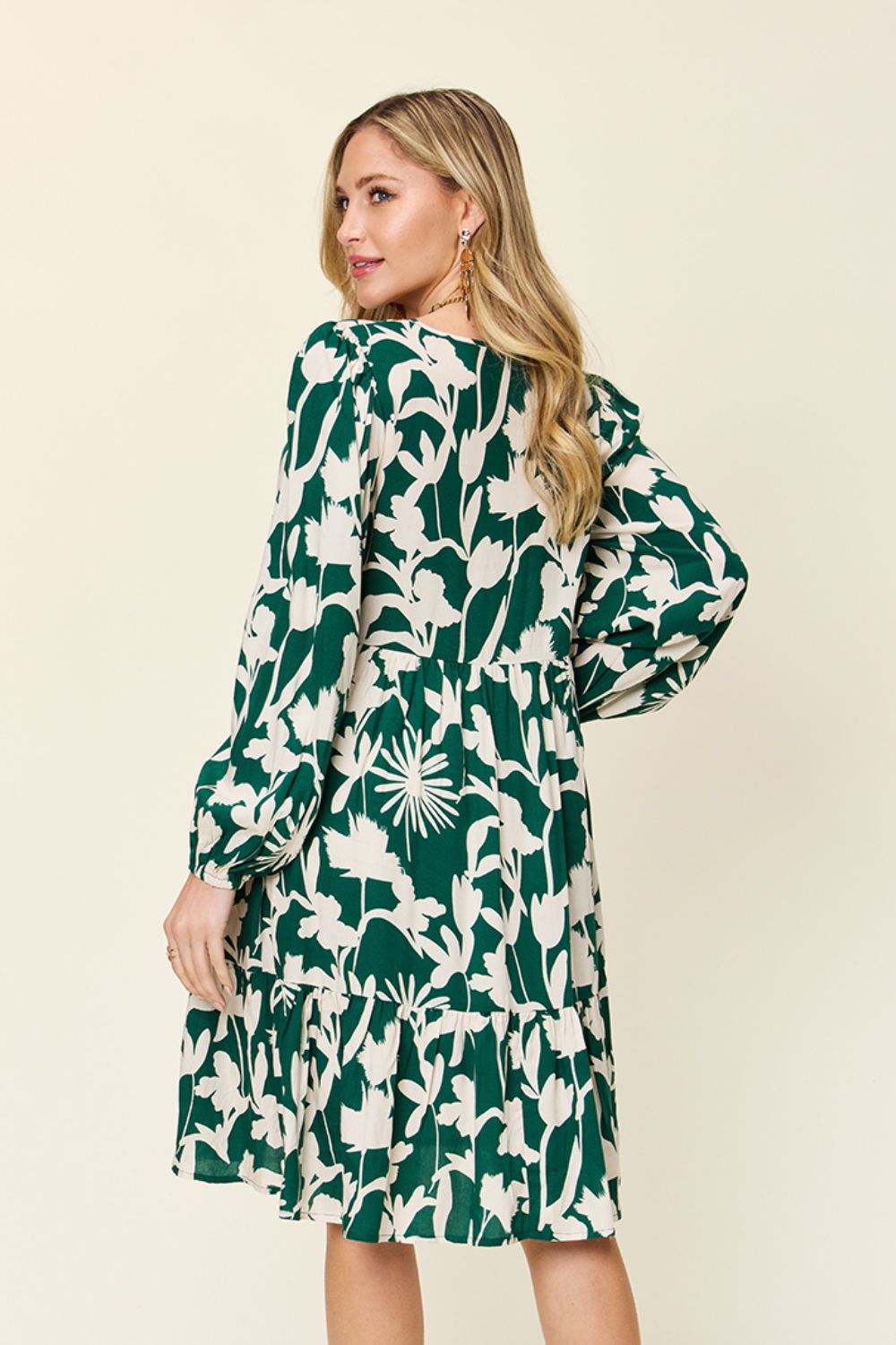 Woman wearing a printed ruffle hem dress with pocket in green and white, showcasing the back design.