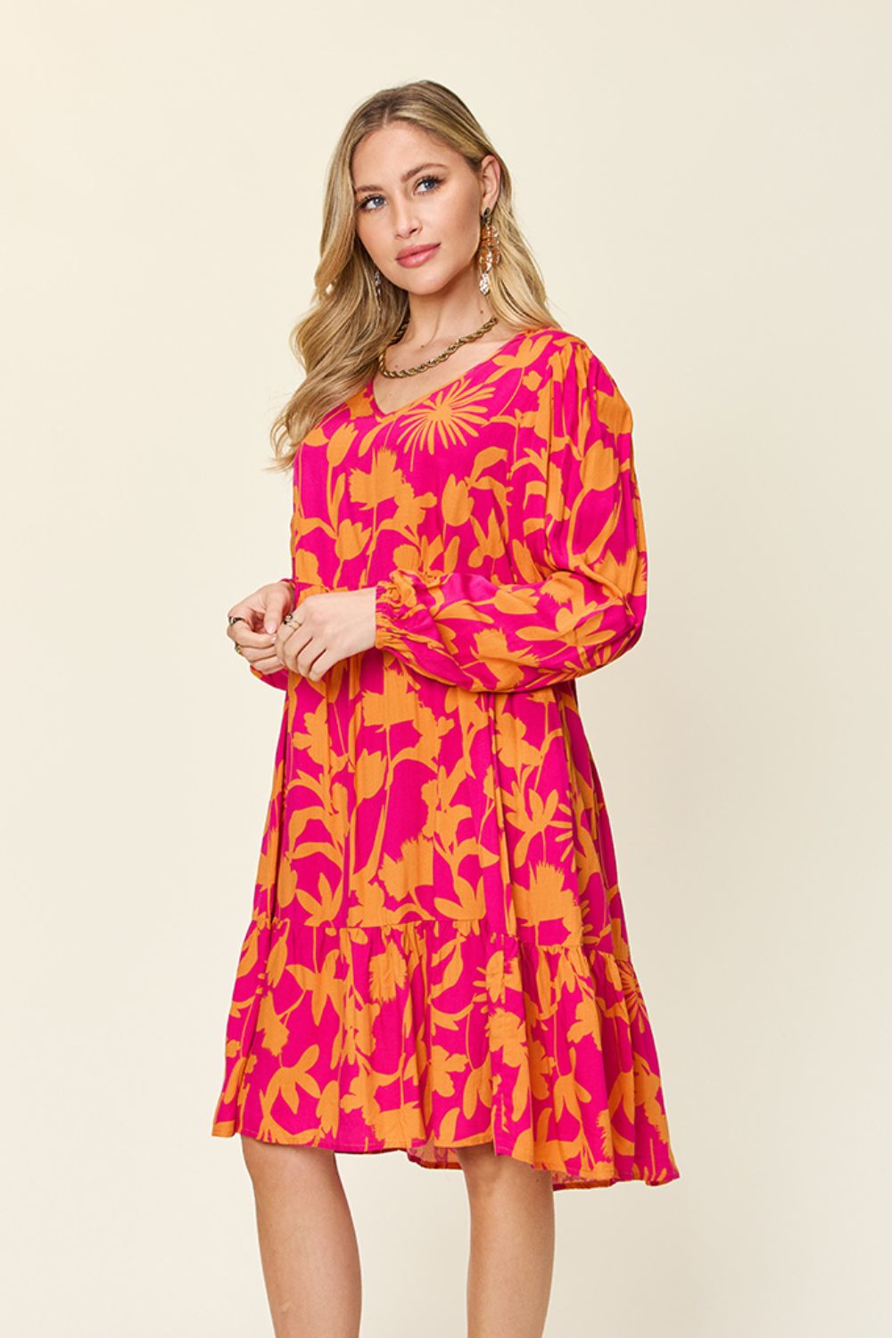 Woman wearing a vibrant pink and orange printed ruffle hem dress with pockets, made from 100% rayon, showcasing a stylish look.