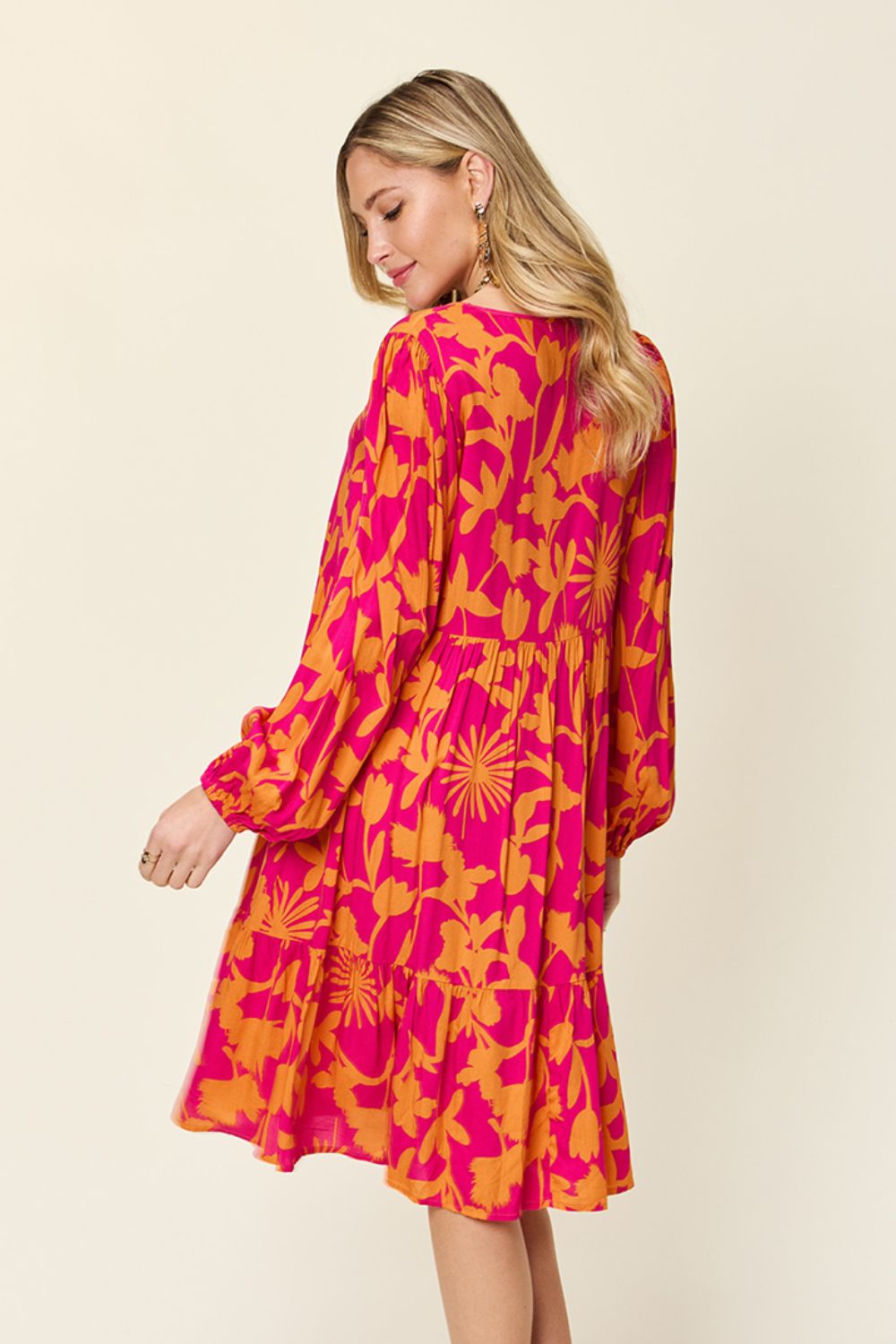 Woman wearing a printed ruffle hem dress with pockets in bright floral pattern, long sleeves, and a flowing silhouette.