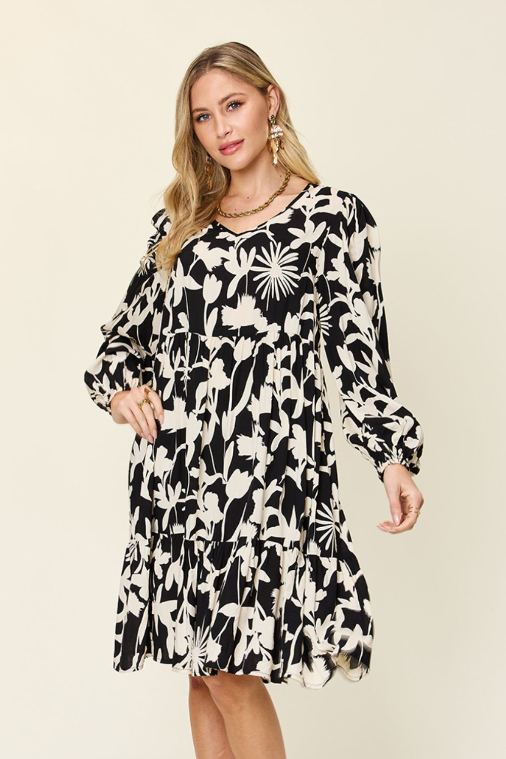 Woman wearing a printed ruffle hem dress with pocket, featuring floral pattern, long sleeves, and elegant design in black and white.