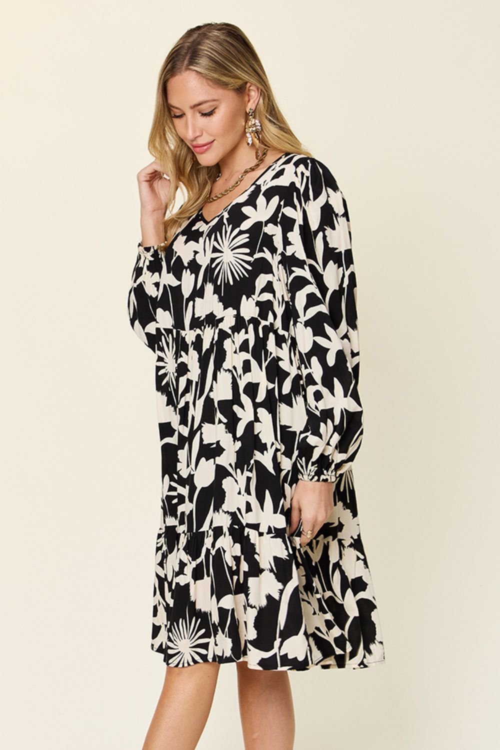 Woman wearing black and white printed ruffle hem dress with pocket, featuring long sleeves and floral pattern.