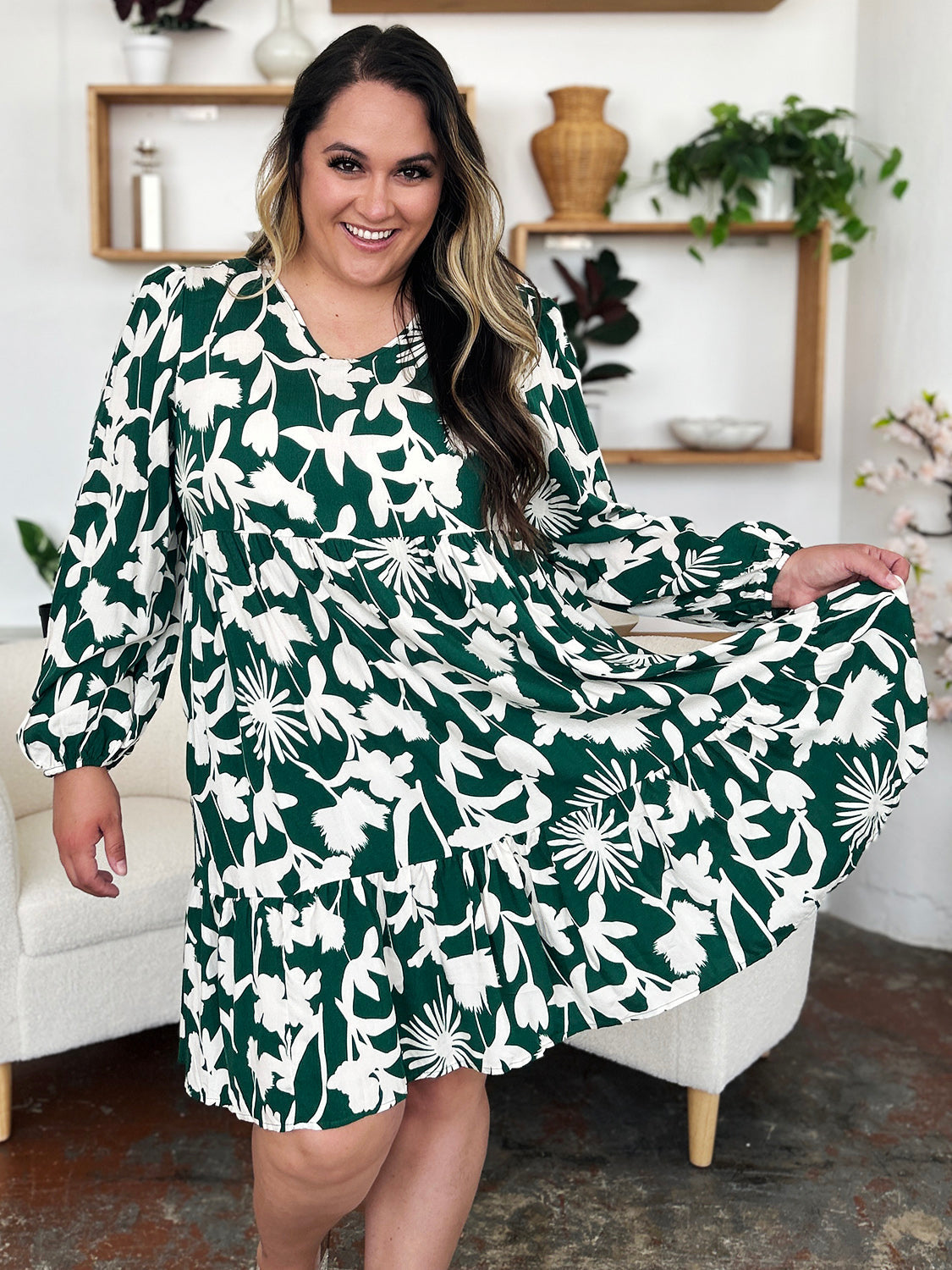 Woman wearing printed ruffle hem dress with pocket in floral pattern, standing in stylish room with plants and modern decor.