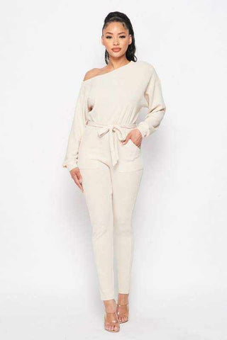 Cream off shoulder waist tie long sleeve jumpsuit made of polyester and spandex, worn by model in stylish pose.