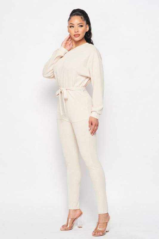 Cream off shoulder long sleeve jumpsuit with waist tie made of polyester and spandex, modeled with elegant heels.