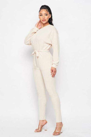 Cream off shoulder long sleeve jumpsuit with waist tie made of polyester and spandex, modeled with elegant heels.
