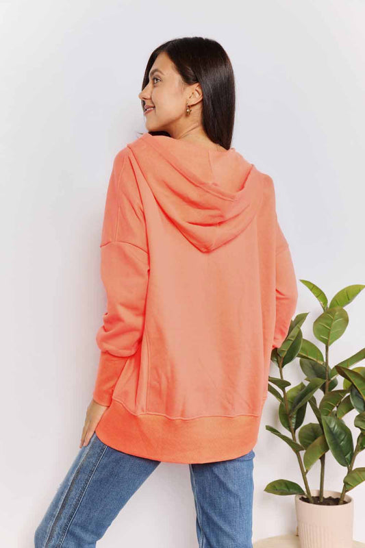 Woman wearing coral quarter-snap dropped shoulder hoodie with hooded neckline, pocketed design, and long regular sleeves.