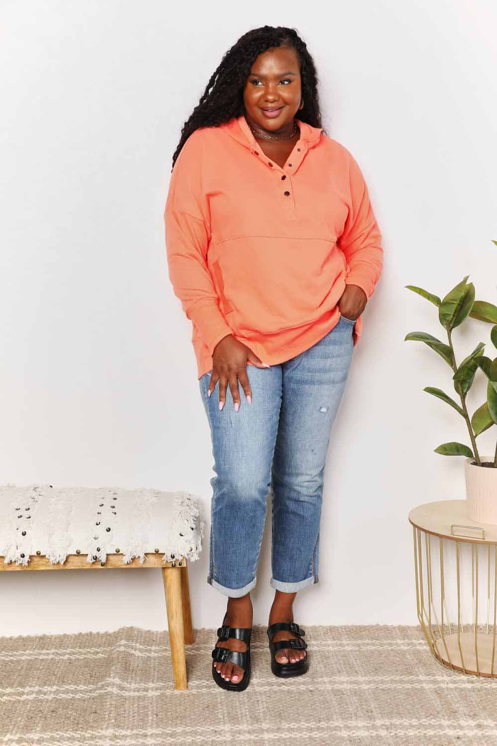 Woman wearing orange quarter-snap dropped shoulder hoodie and jeans, showcasing casual style with buttoned neckline and pockets.