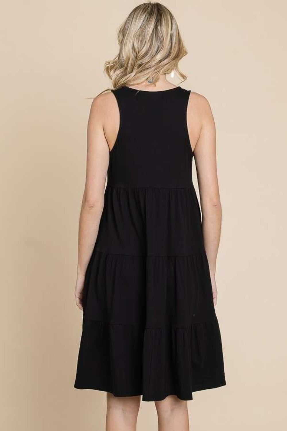 Woman wearing black racerback tiered tank dress with ruched design, made of cotton-rayon blend, slightly stretchy and opaque.