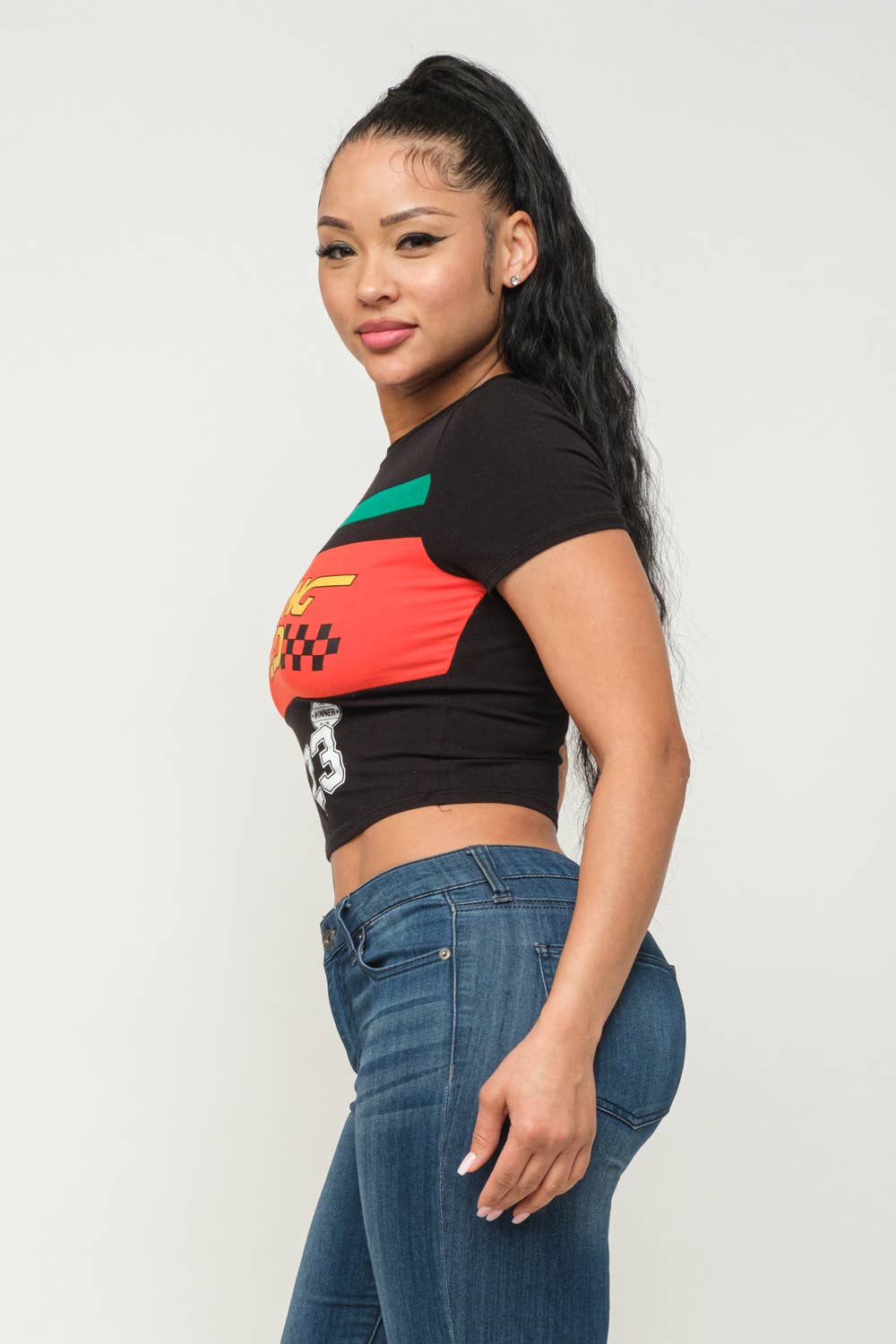 Woman wearing a racing speed screen print crop top with round neck and short sleeves, paired with jeans.