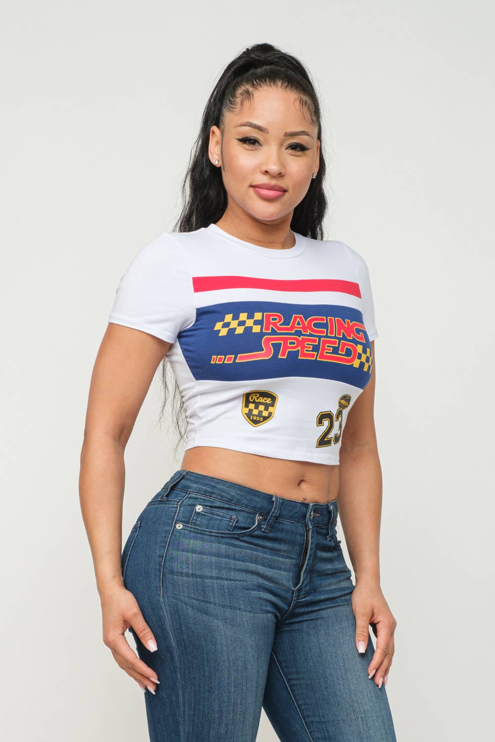 Woman wearing a "Racing Speed" screen print short sleeve crop top, cotton spandex blend, showcasing casual style with jeans.