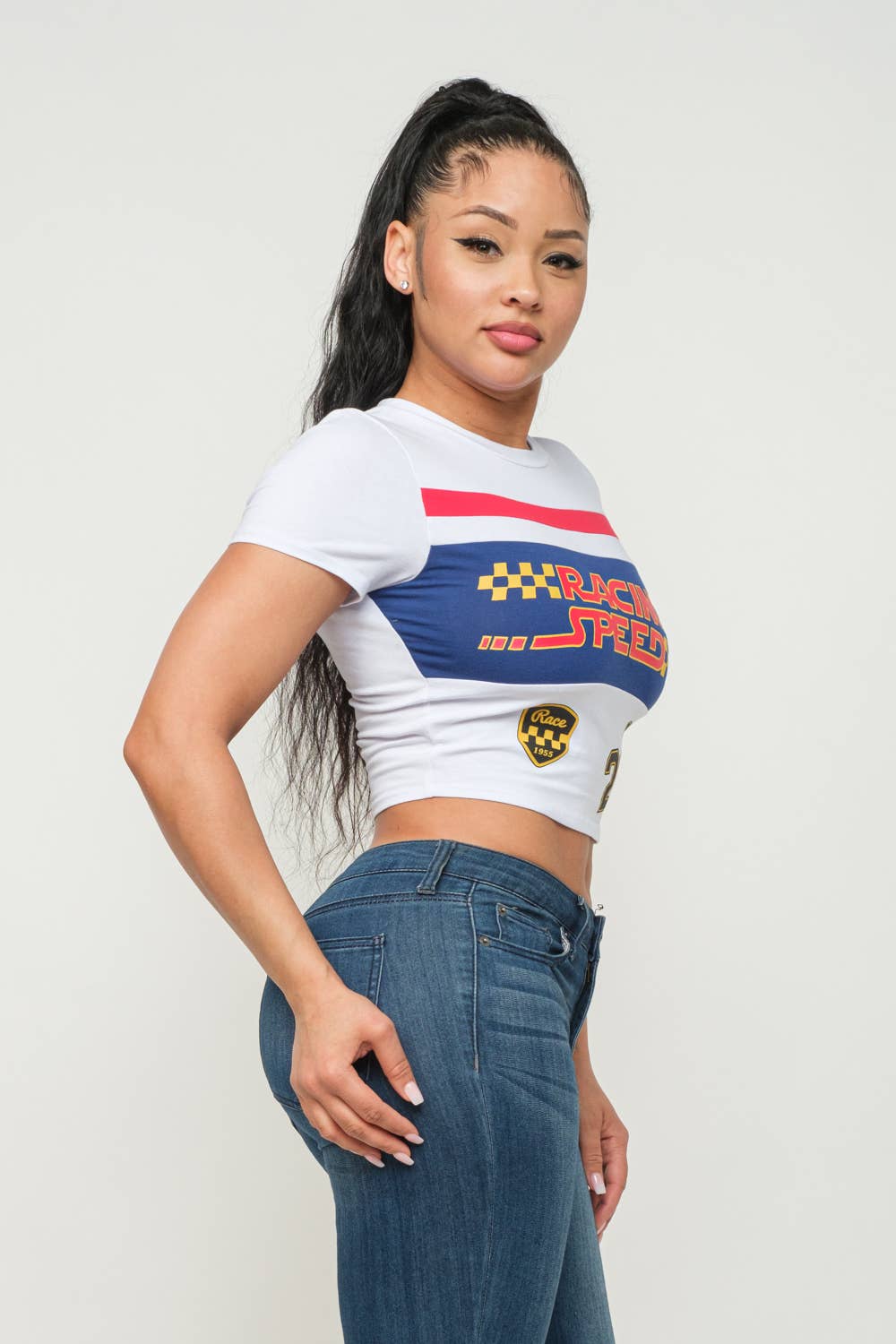 Woman wearing a white crop top with "Racing Speed" print and blue details, paired with blue jeans.