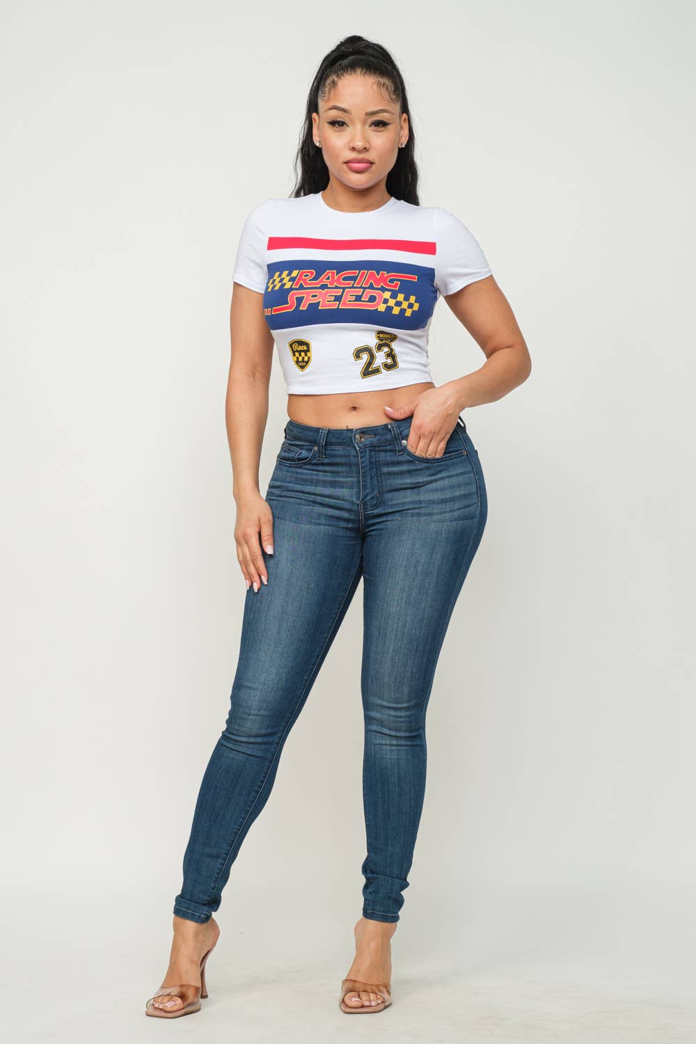 Woman wearing white Racing Speed screen print crop top paired with denim jeans and heels.