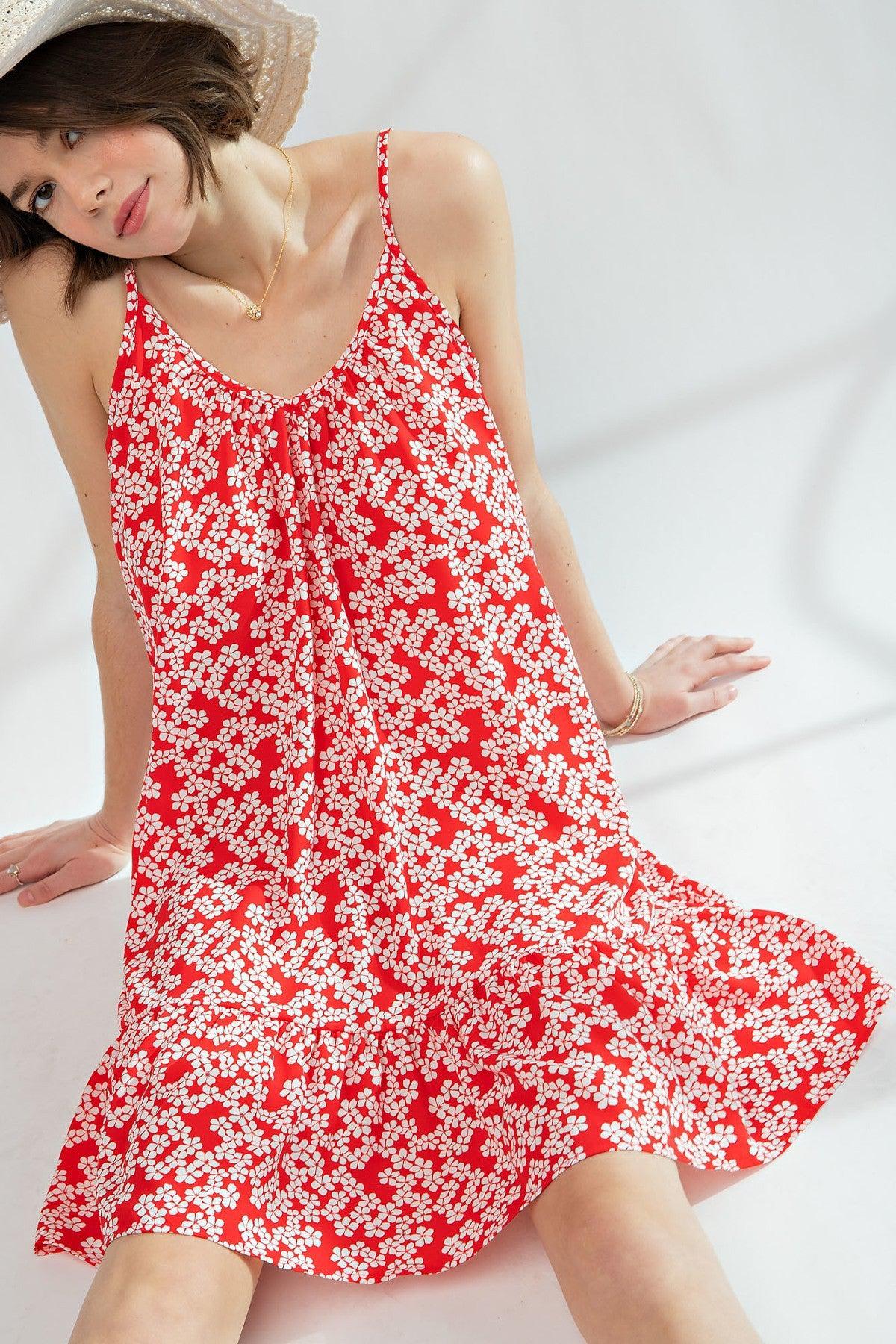 Woman wearing red floral printed wool peach cami dress with ruffled bottom and spaghetti straps, sitting gracefully.