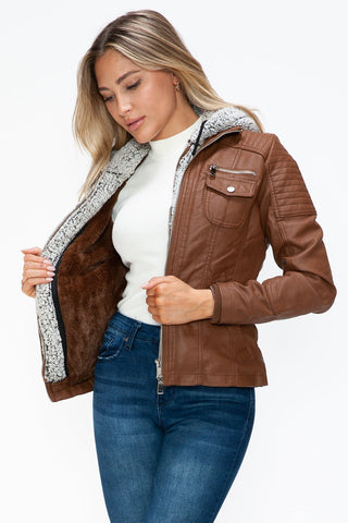 Woman wearing removable faux layered multi-pocket brown jacket with fuzzy hood and white tee.