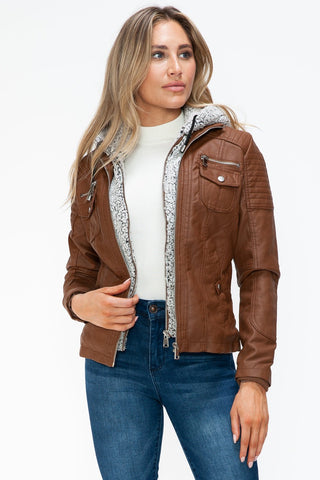 Woman wearing a removable faux layered multi-pocket jacket with a fuzzy hood, showcasing its stylish design and brown pleather material.