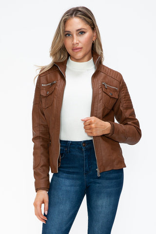 Removable faux layered brown jacket with multiple pockets and fuzzy hood, worn by a model in white top and jeans.