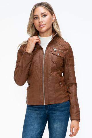 Removable faux layered multi-pocket jacket with fuzzy hood, brown pleather, zip front, worn by model, casual style.
