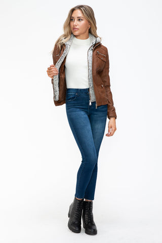 Woman wearing brown removable faux layered jacket with fuzzy hood and multi-pockets, styled with jeans and black boots.