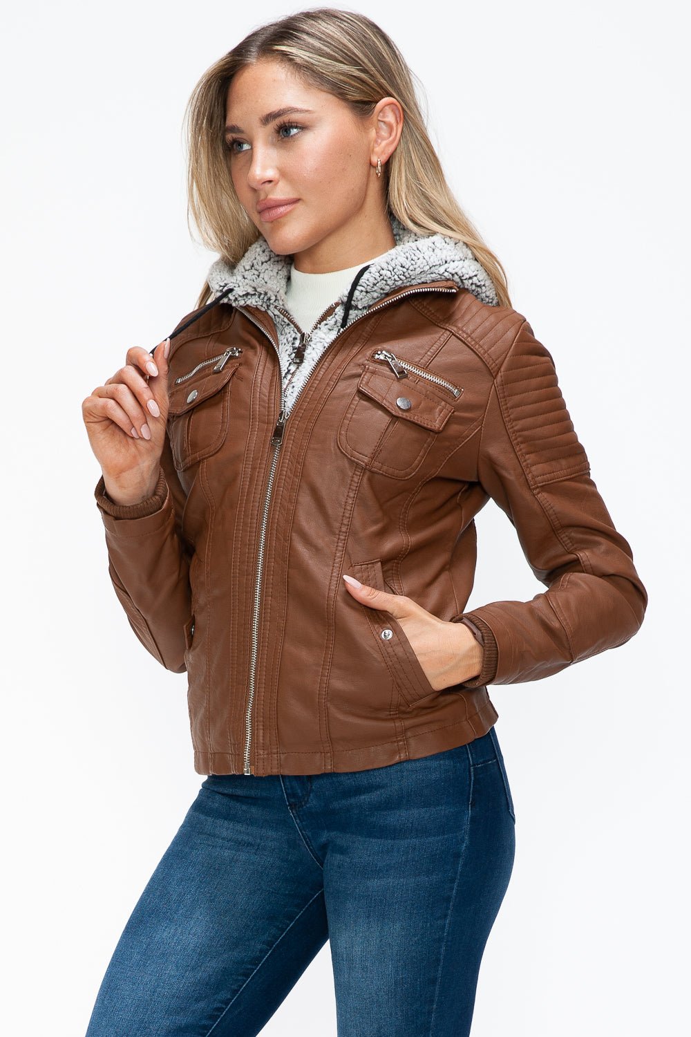 Woman wearing a brown faux leather jacket with multiple pockets and a fuzzy hood, featuring a removable layered design.