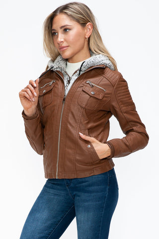 Woman wearing a brown faux leather jacket with multiple pockets and a fuzzy hood, featuring a removable layered design.