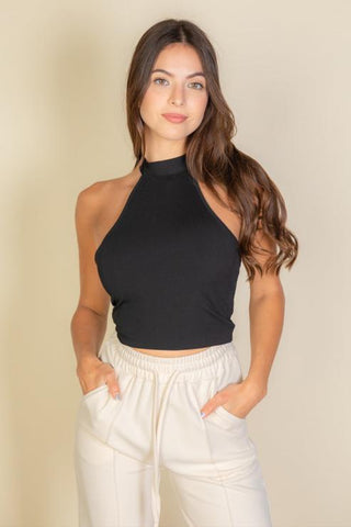 Woman wearing a black ribbed halter neck backless top and light pants, showcasing stretchy soft fabric, perfect for casual style.