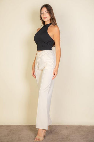 Model wearing a black ribbed halter neck backless top paired with cream trousers in studio setting.