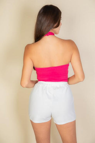 Woman wearing a pink ribbed halter neck backless top paired with white shorts, showcasing soft and stretchy fabric fit.