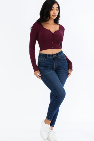 Woman wearing a ribbed long sleeve snap button down crop top in burgundy with jeans and white sneakers.